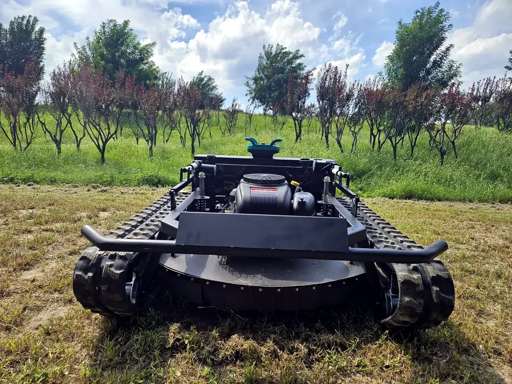 Tracked mower on grass in a sloped orchard setting